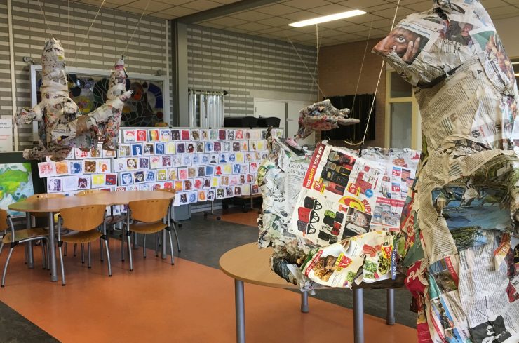 Klaslokaal met papier-maché objecten en een wand met portrettekeningen