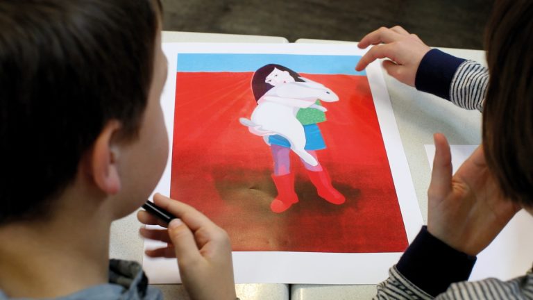 Twee leerlingen bekijken samen een kunstwerk van een meisje dat een reuzekonijn vasthoudt