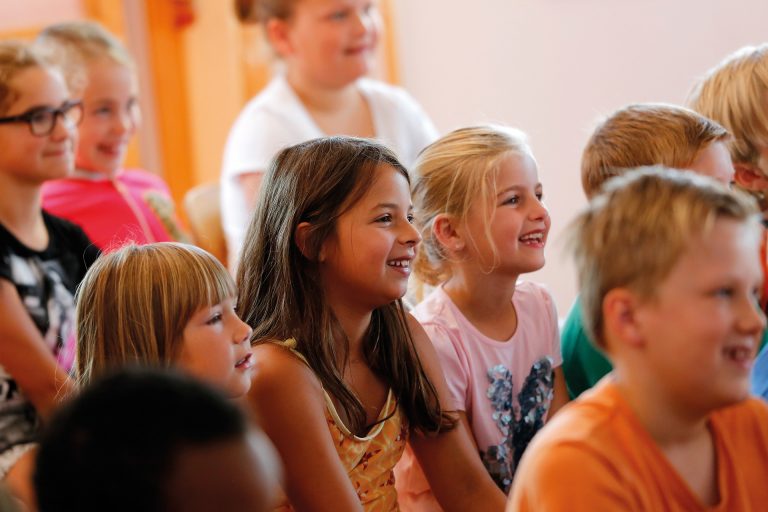 Kinderen kijken naar een theatervoorstelling en lachen