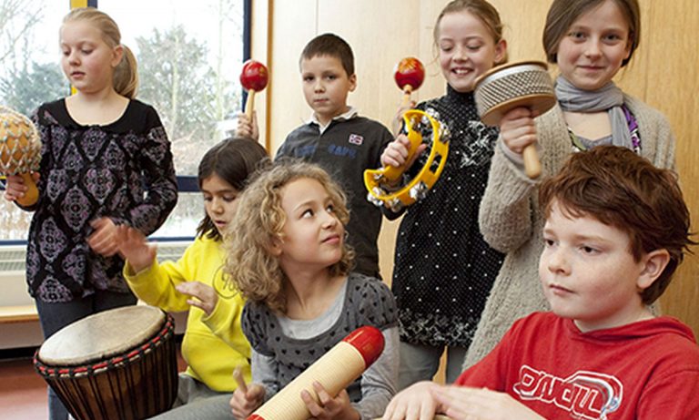 Groepje leerlingen maakt muziek met verschillende instrumenten zoals trommel, sambaballen en tamboerijn