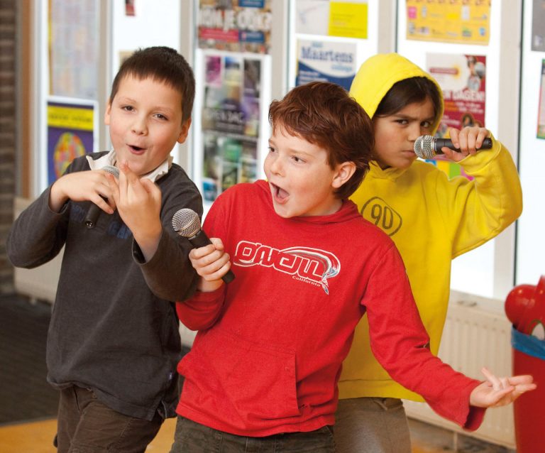 Drie jongens zingen en rappen met microfoons in hun hand