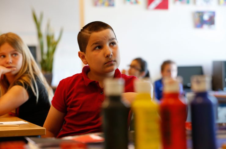 Jongen kijkt aandachtig naar docent, voor hem staan potten verf in verschillende kleuren.