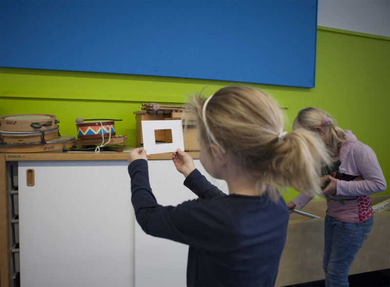Leerling in de klas bekijkt voorwerpen doorheen een kadertje tijdens een creatieve les over Van Gogh