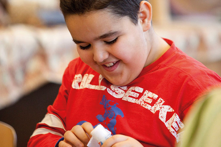 Jongen met rood shirt lacht terwijl hij lijm op papier aanbrengt