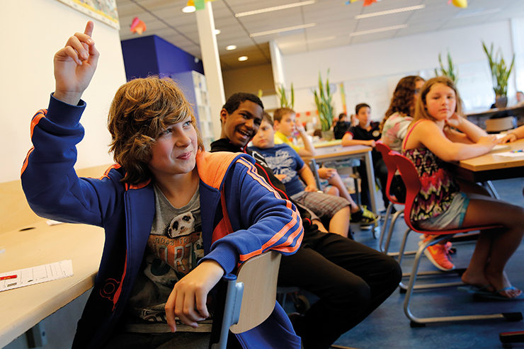 Jongen in blauw-oranje hoodie steekt zijn vinger op terwijl medeleerlingen toekijken