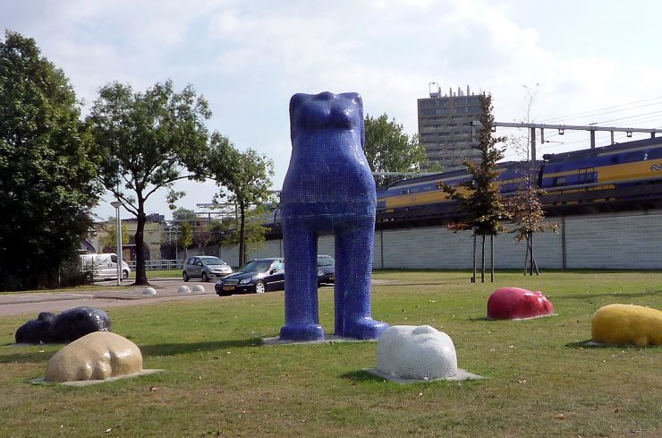 Kunstwerk door Chris Ripken van een staand blauw vrouwenlichaam zonder hoofd, om haar heen liggen hoofden in verschillende kleuren