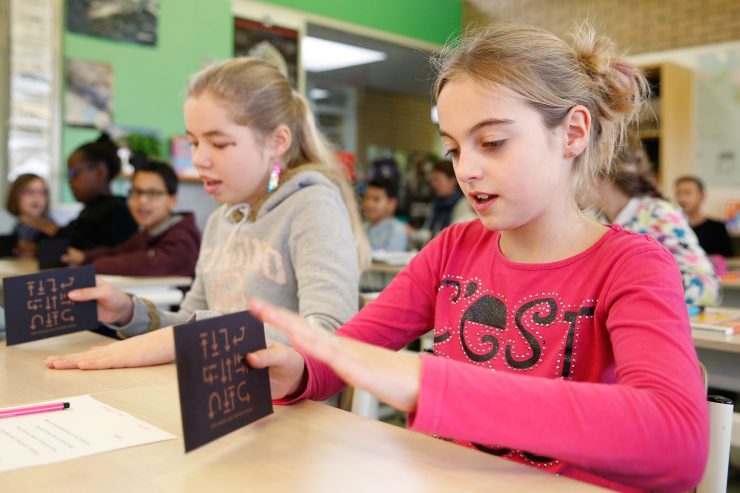 Twee leerlingen maken ritmes met een kartonnen kaartje op hun lessenaar