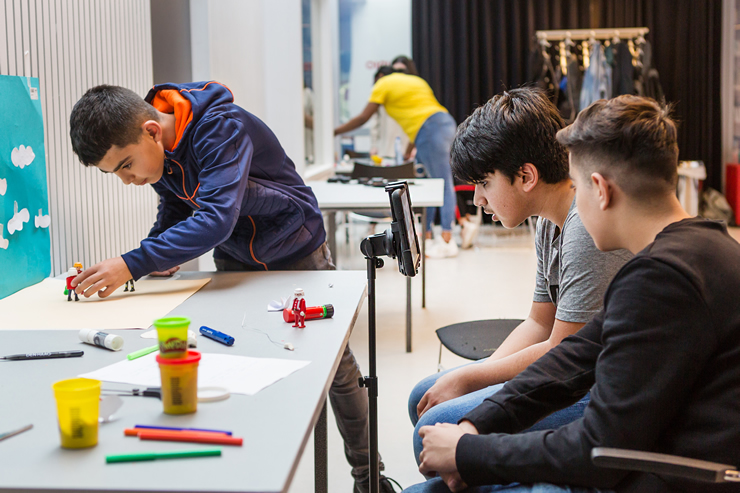 Drie leerlingen werken aan een stopmotion filmpje en plaatsen playmobile-poppetjes tegen een zelfgemaakte achtergrond
