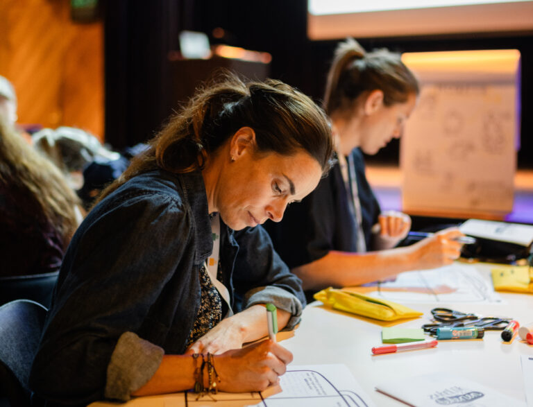 Vrouw schrijft op papier, zit aan tafel.