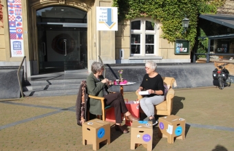 Twee vrouwen breien en praten in de zon voor het pand van De Spreekkamer van de Stad in Gorinchem waar kunst en bewoners dichter bij elkaar worden gebracht