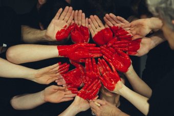 Groep mensen houdt handpalmen als een soort canvas dichtbij elkaar terwijl iemand er met rode verf een groot hart op schildert