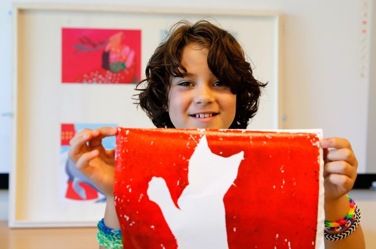 Een jonge deelnemer van cultuuronderwijsprogramma Doe|Kunst houdt trots zijn werk omhoog