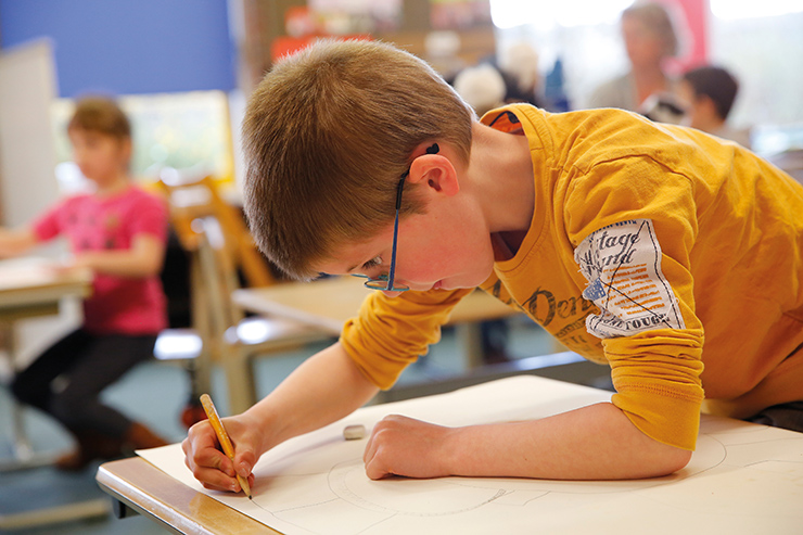 Jongen met geel shirt en blauwe bril maakt tekening op groot vel papier