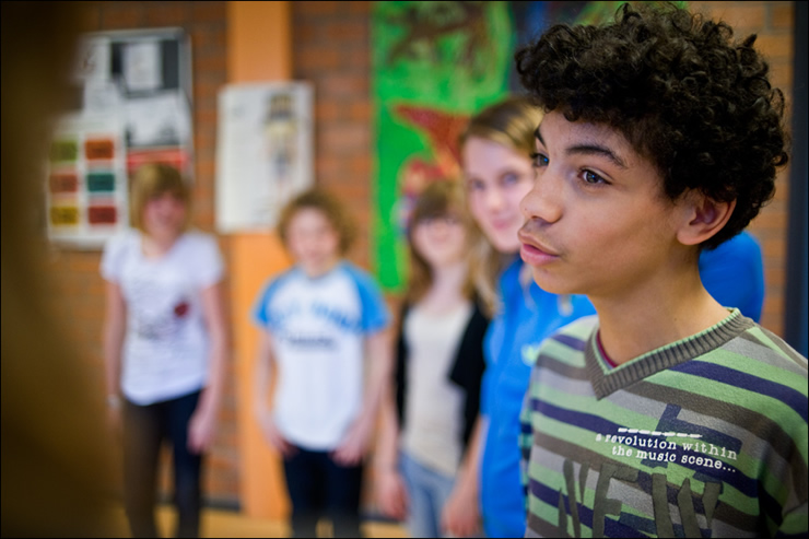 Jongen met donkere krullen en groen gestreepte trui is aan het woord tijdens theaterworkshop