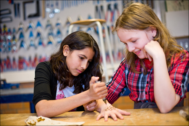 Meisje maakt henna-tatoeage op de hand van haar klasgenoot in het handvaardigheidlokaal