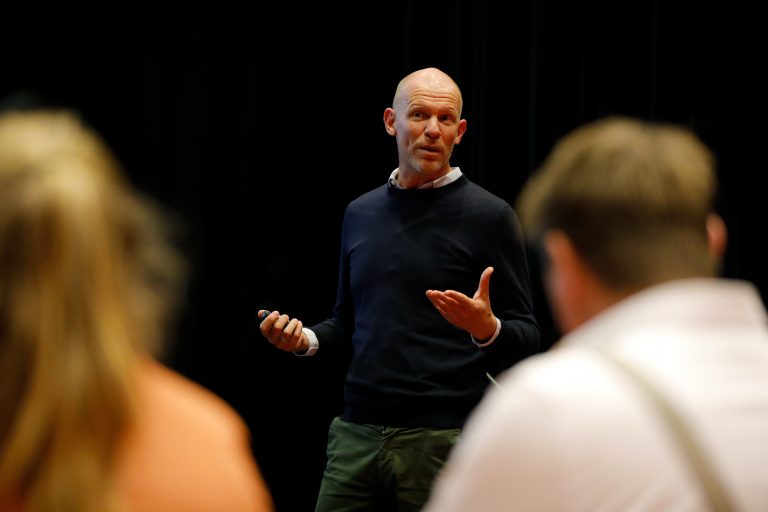 Kale man in donkerblauwe trui geeft een presentatie aan een groep mensen tijdens het subsidiekamp cultuurparticipatie