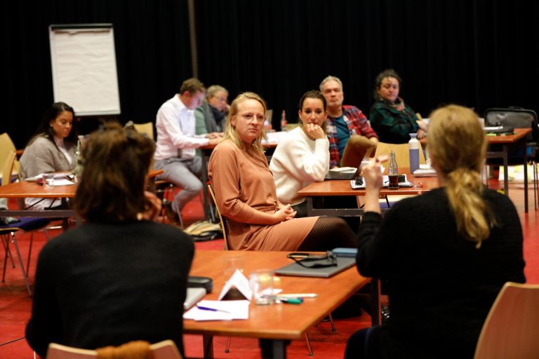 Deelnemers van Subsidiekamp Cultuurparticipatie zitten achter tafeltjes en luisteren naar presentatie