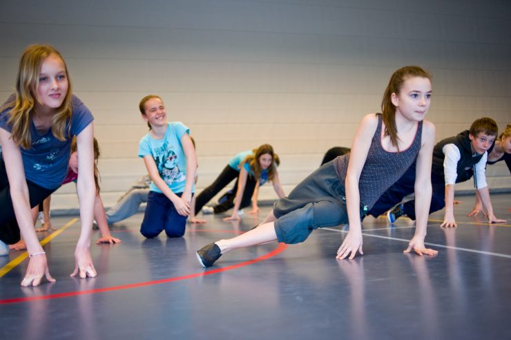 Tieners doen mee aan breakdanceworkshop in een gymzaal