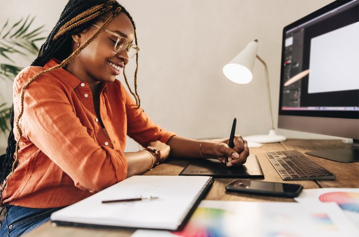 Vrouw met bril en lange kleine vlechtjes werkt met een digitale pen op een touchpad van een computer