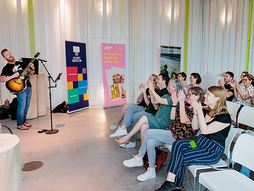 Man met gitaar is net klaar met zijn optreden voor docenten die hard applaudisseren