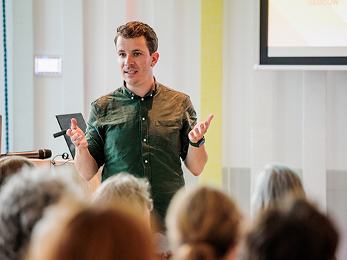 Man in groen overhemd met korte mouwen staat voor een groep docenten en geeft een presentatie