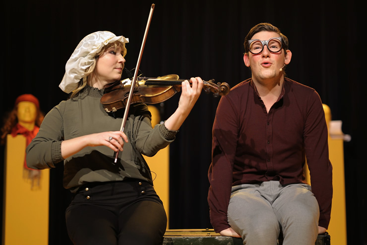 Max en de minipiano Vrouw met witte kap speelt viool zit naast man met donkere bril die zingt