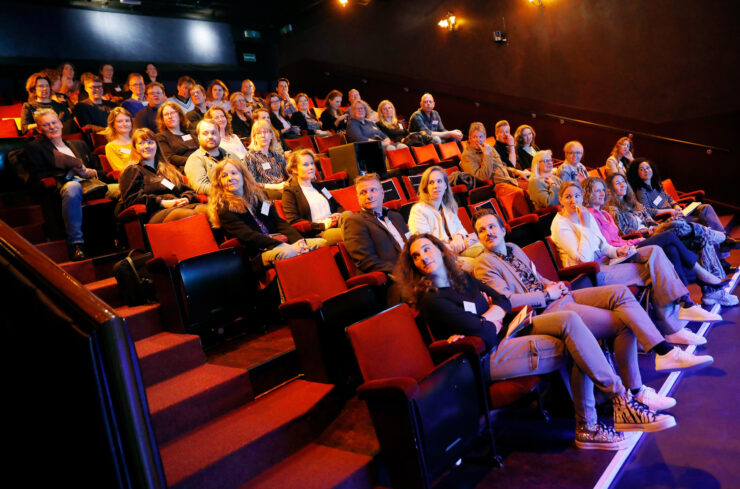 Mensen zitten in een theaterzaal en kijken allen dezelfde kant op.