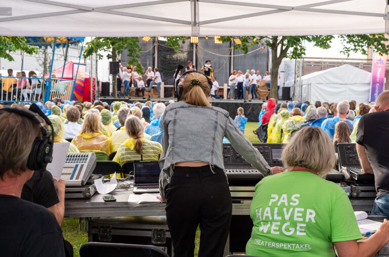 Blik vanaf de techniektafel op het podium waar een groep amateur-acteurs een voorstelling speelt