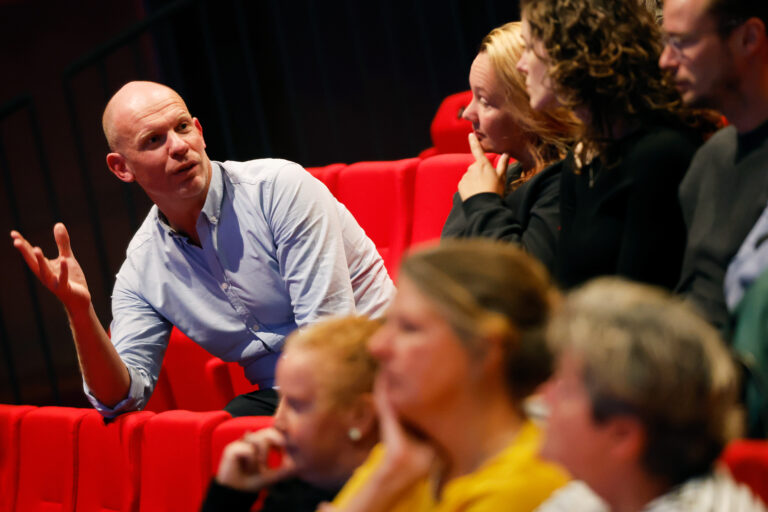 Een man licht zijn punt toe terwijl de rest van het publiek aandachtig luistert