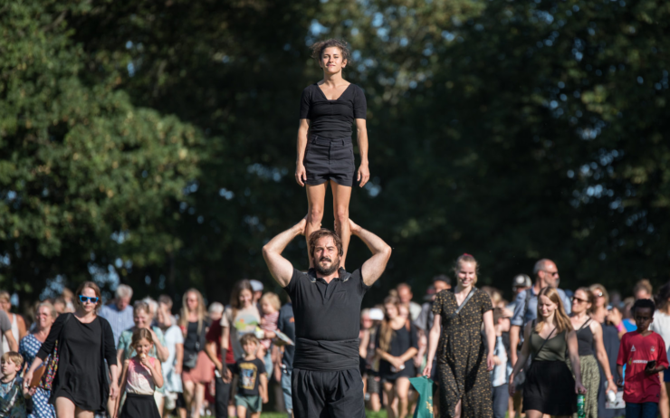 Vrouw staat op schouders van man. Publiek op de achtergrond.