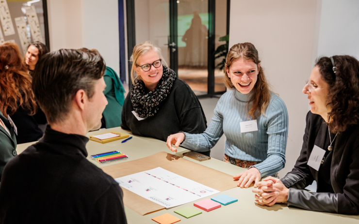 Volwassenen zitten lachend aan een tafel tijdens een workshop.