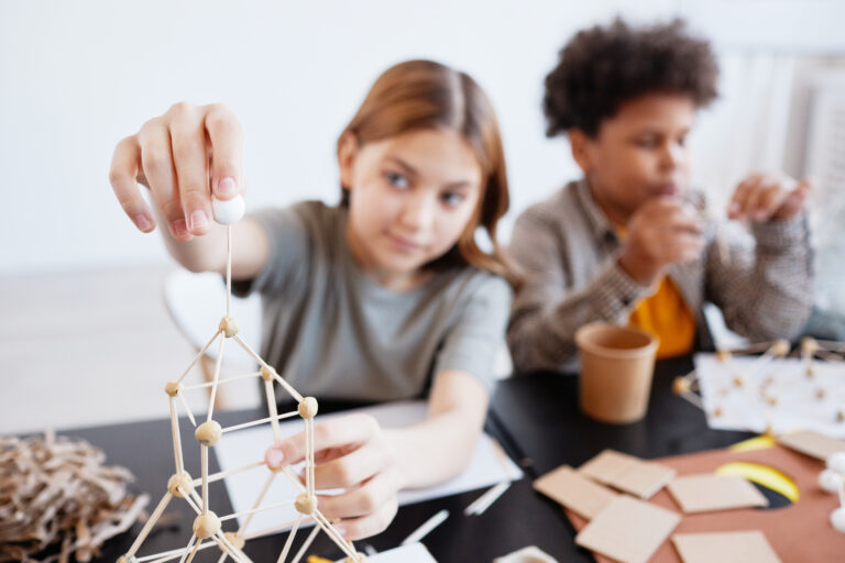 Kinderen bouwen een toren van stokjes aan tafel.