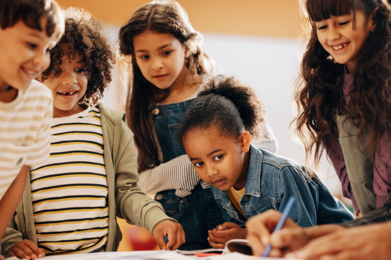 Jonge kinderen kijken toe hoe iemand iets opschrijft of tekent.