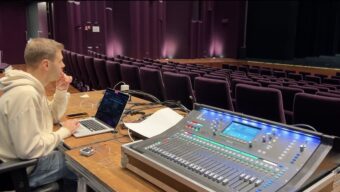 Iemand achter techniektafel in lege theaterzaal.