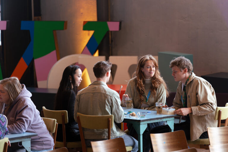 Jongeren zitten aan een tafel en praten met elkaar.