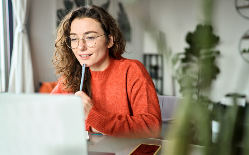 Vrouw met krullen zit achter laptop in huiskamer.